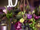 a colorful fall wedding centerpiece of purple and neutral blooms and greenery, candles and a table number over the arrangement