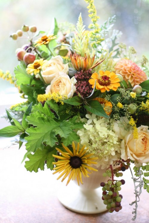 a bright fall wedding centerpiece of bold and neutral blooms and lots of textural greenery is very textural and catchy