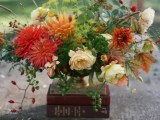 a bright fall wedding centerpiece of orange, red and rust blooms, creamy flowers and textural greenery