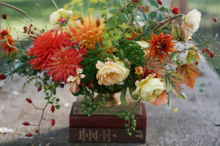 A bright fall wedding centerpiece of orange, red and rust blooms, creamy flowers and textural greenery