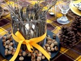 a creative fall wedding centerpiece of a black plate, nuts and acorns, a candleholder covered with sticks and branches and a yellow ribbon