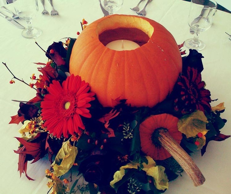 A bright fall wedding centerpiece of bold blooms, dark foliage, twigs and a cutout pumpkin with a candle inside
