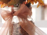a rustic fall wedding centerpiece of a jar filled with walnuts, bright blooms and a sheer brown ribbon bow
