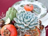 a creative fall wedding centerpiece of fruit, artichokes, a large succulent and berries looks yummy and fall-like