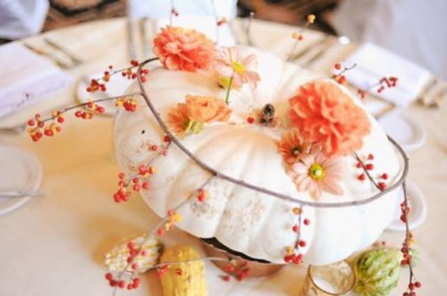 a white pumpkin with bright blooms inserted into it and some berries on a twig is a cool fall wedding centerpiece