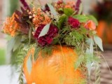 a pumpkin with greenery and ferns and bold blooms and berries is a cool fall wedding centerpiece
