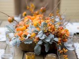 a wooden bowl with pale foliage, fruits and branches with berries is a simple and cool rustic fall wedding centerpiece