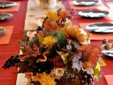 a pumpkin with bright blooms, dried foliage, berries and fruit is a nice fall wedding centerpiece idea