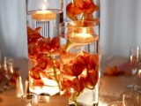 tall glasses with bright blooms and floating candles on top and candles around for a fall wedding