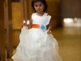 a white wide strap A-line tulle flower girl dress with an orange sash and a blue flower is very pretty