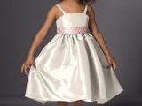 a neutral shiny flower girl dress with straps, a pink sash and a pleated skirt is a stylish and cute idea