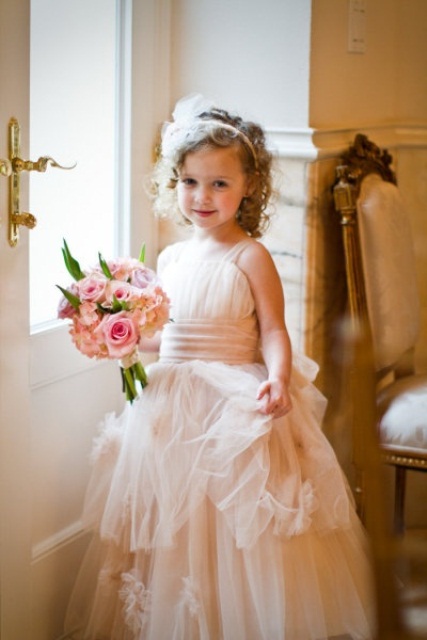 a blush tulle flower girl dress with a pink sash and a pink headpiece for a chic and beautiful look
