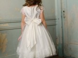 a white A-line flower girl dress with a pleated skirt, a large bow on the back and cap sleeves