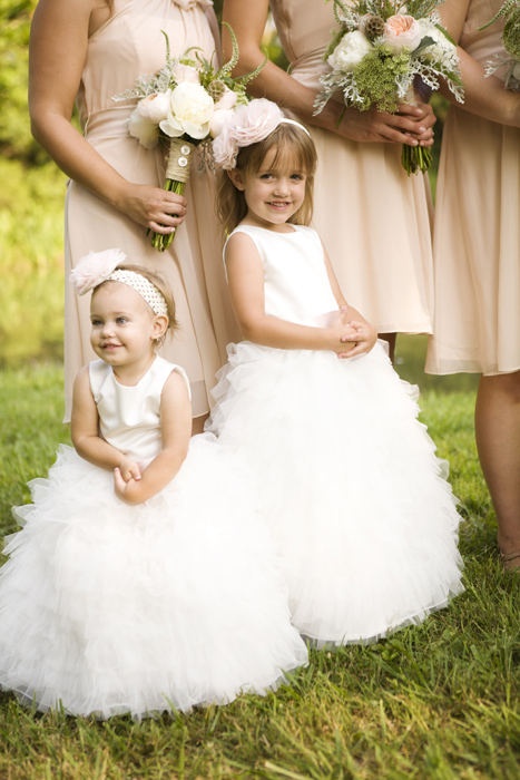 white sleeveless flower girl dresses with plain bodices, ruffle layered skirts and oversized fabric flower headpieces