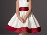 a white A-line flower girl dress with a burgundy sash and a burgundy trim on the edge for a classic and rather formal look