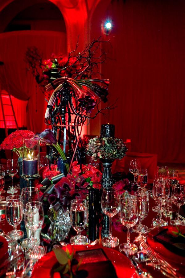 A dramatic Halloween wedding centerpiece in black and red, with branches, red blooms and black candles plus floral arrangements