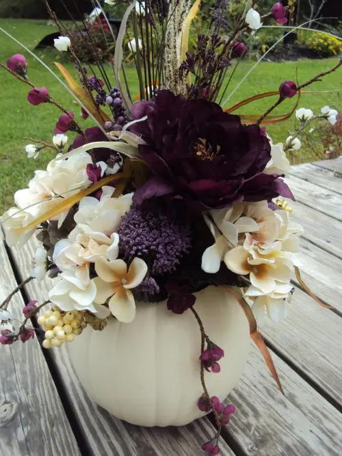 a fall-inspired and Halloween wedding centerpiece of a white pumpkin, neutral and purple blooms, berries and branches