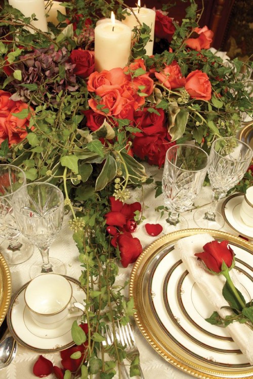a chic Valentine's Day wedding table with greenery, red and burgundy roses, gold rimmed plates, red roses and crystal glasses