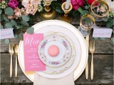 a beautiful Valentine’s Day wedding table with a lush greenery, blush and fuchsia runner, white candles in gold candleholders, gold cutlery and stacked plates plus pink menus