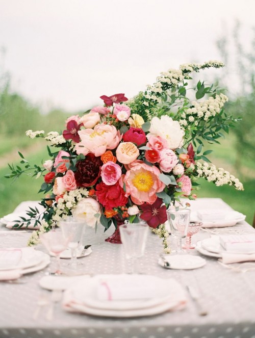 a grey polka dot tablecloth, white porcelain, blush napkins and glasses and a bold floral arrangement with greenery and grasses