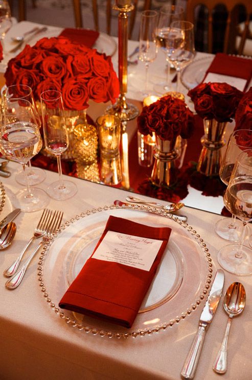 a refined white, red and gold Valentine's wedding tablescape with a shiny table runner, burgundy napkins, glam gold vases and candleholders and red roses
