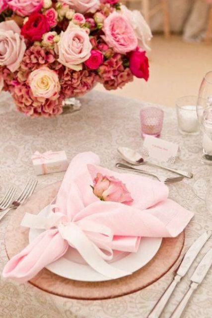a sweet and romantic Valetine's Day wedding table with a printed tablecloth, a pink glass charger and light pink linens, a chic bold pink and mauve floral arrangement is beautiful