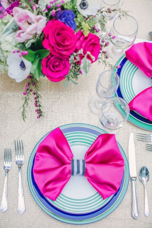 a super bright Valentine's Day wedding table with a silver tablecloth, hot pink napkins, electric blue plates, hot pink and bright blue blooms is ultra-modern