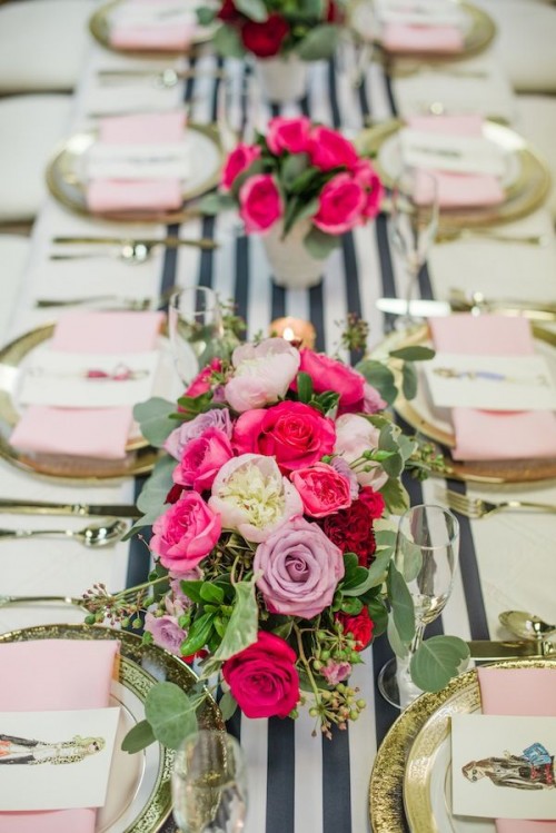 an elegant and glam Valentine's wedding table with a striped runner, gold chargers and cutlery and pink napkins plus bold pink, fuchsia and lavender bloom arrangements