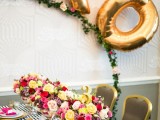 a bold Valentine’s Day wedding tablescape with a striped tablecloth, bold fuchsia table runners and napkins, bold floral arrangement, a greenery arch with gold XO letters
