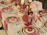 a romantic blush, pink and white Valentine’s Day wedding tablescape with a vintage tablecloth, gold rimmed chargers and cutlery, blush adn pink blooms in balls, candles and a refined floral table runner