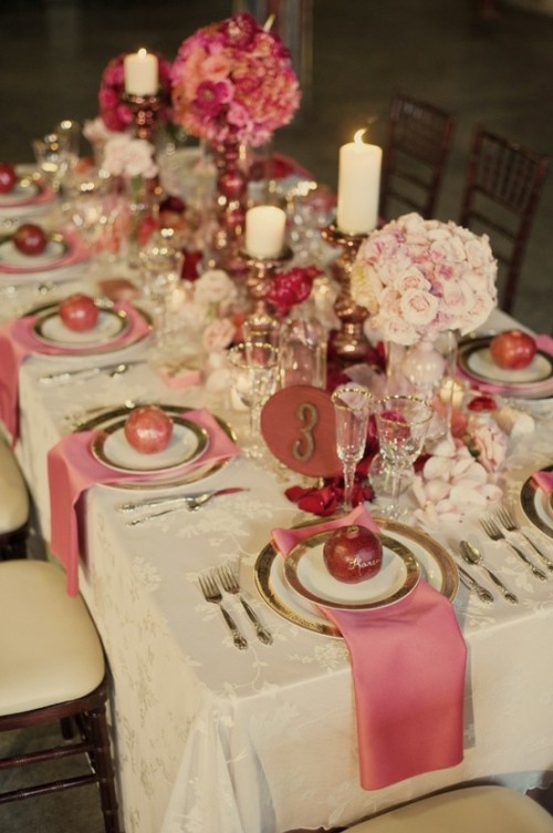 a romantic blush, pink and white Valentine's Day wedding tablescape with a vintage tablecloth, gold rimmed chargers and cutlery, blush adn pink blooms in balls, candles and a refined floral table runner