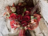 a bold red winter wedding bouquet with dried herbs and large feathers plus a red wrap