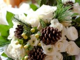 a rustic winter wedding bouquet with white blooms, greenery, berries and pinecones