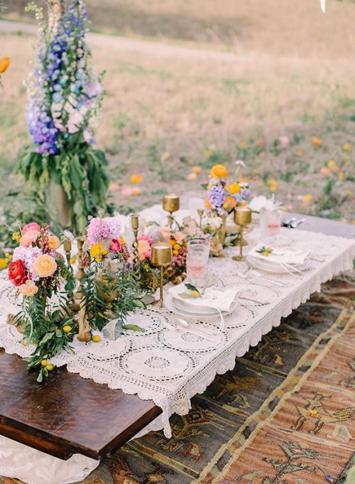 a macrame tablecloth, super colorful blooms, gold candle holders and gold cutlery