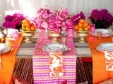 a colorful boho tablescape with bright pink and orange textiles, bright blooms and citrus and gold touches