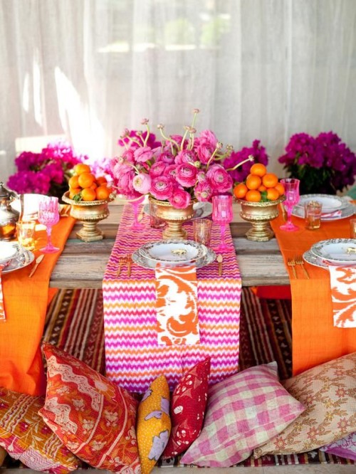 a colorful boho tablescape with bright pink and orange textiles, bright blooms and citrus and gold touches
