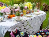 a boho meets vintage tablescape with a macrame tablecloth, bright blooms and fruits, colorful plates and cups
