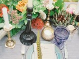 a boho table setting with an aqua plate, colored glasses, a bright floral and greenery centerpiece and lots of candles