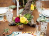 a bright tablescape with colorful placemats, driftwood, colorful florals, candles and air plants