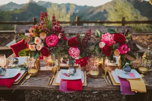 a lush and colorful tablescape with bright florals, textiles, gilded touches and candle lanterns