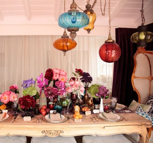 a colorful tablescape with bright lamps hanging down, colorful florals, fruits and colored glasses