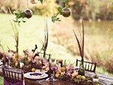 a boho tablescape done with a moss and bloom runner, feathers in bottles, colorful textiles and suspended ornaments with petals
