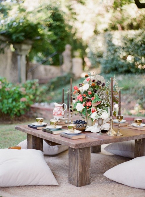 a low picnic table with candles, a lush floral centerpiece, books instead of placemats and vintage teacups