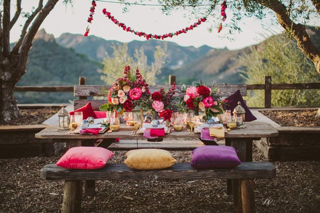 A bright boho tablescape with colorful pillows and florals, gilded touches, candle lanterns and garlands
