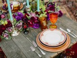 a colorful tablescape with bright florals, glasses, candles and gilded plates and chargers