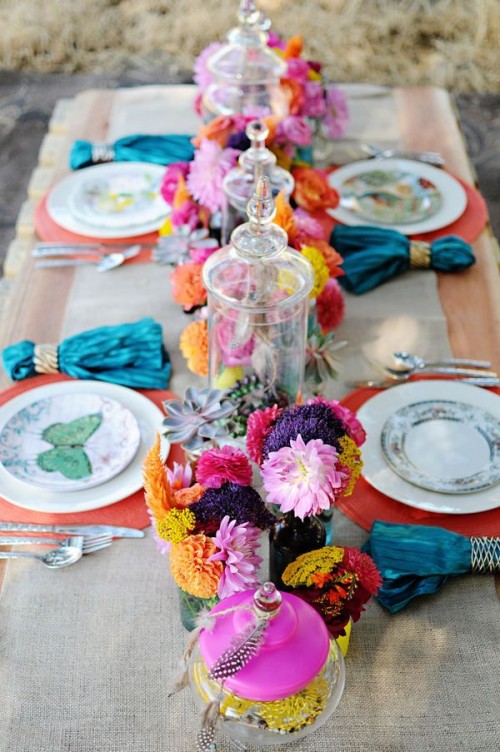 a colorful tablescape with a burlap tablecloth, colorful plates and napkins plus colorful florals