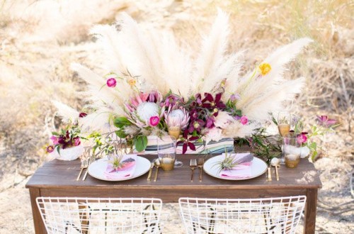 a boho chic table setting with bright florals and pampas grass, tie dye napkins and candles
