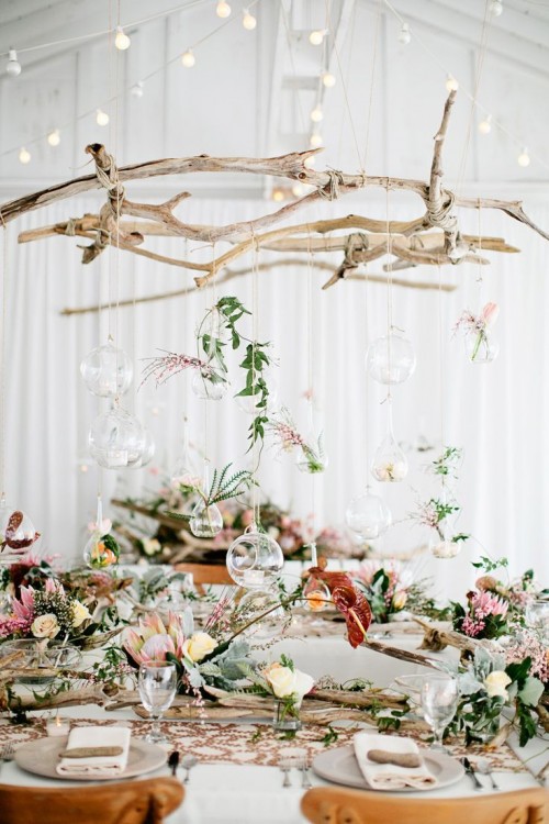 a boho tablescape with with floral decor, driftwood over the table and glass bubbles with blooms