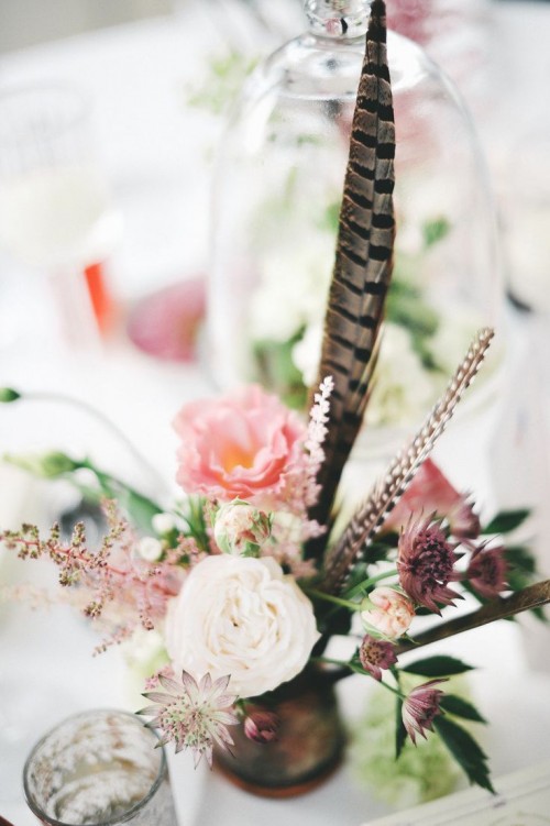 a dimensional floral wedding centerpiece with a couple of feathers and some foliage for a boho wedding