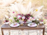 a lush and bright boho wedding centerpiece with dark blooms, greenery and pampas grass for a boho wedding